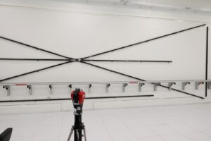 W pomieszczeniu laboratoryjnym, na białej ścianie, rozwieszone różnej długości cienkie listwy do pomiarów długości.