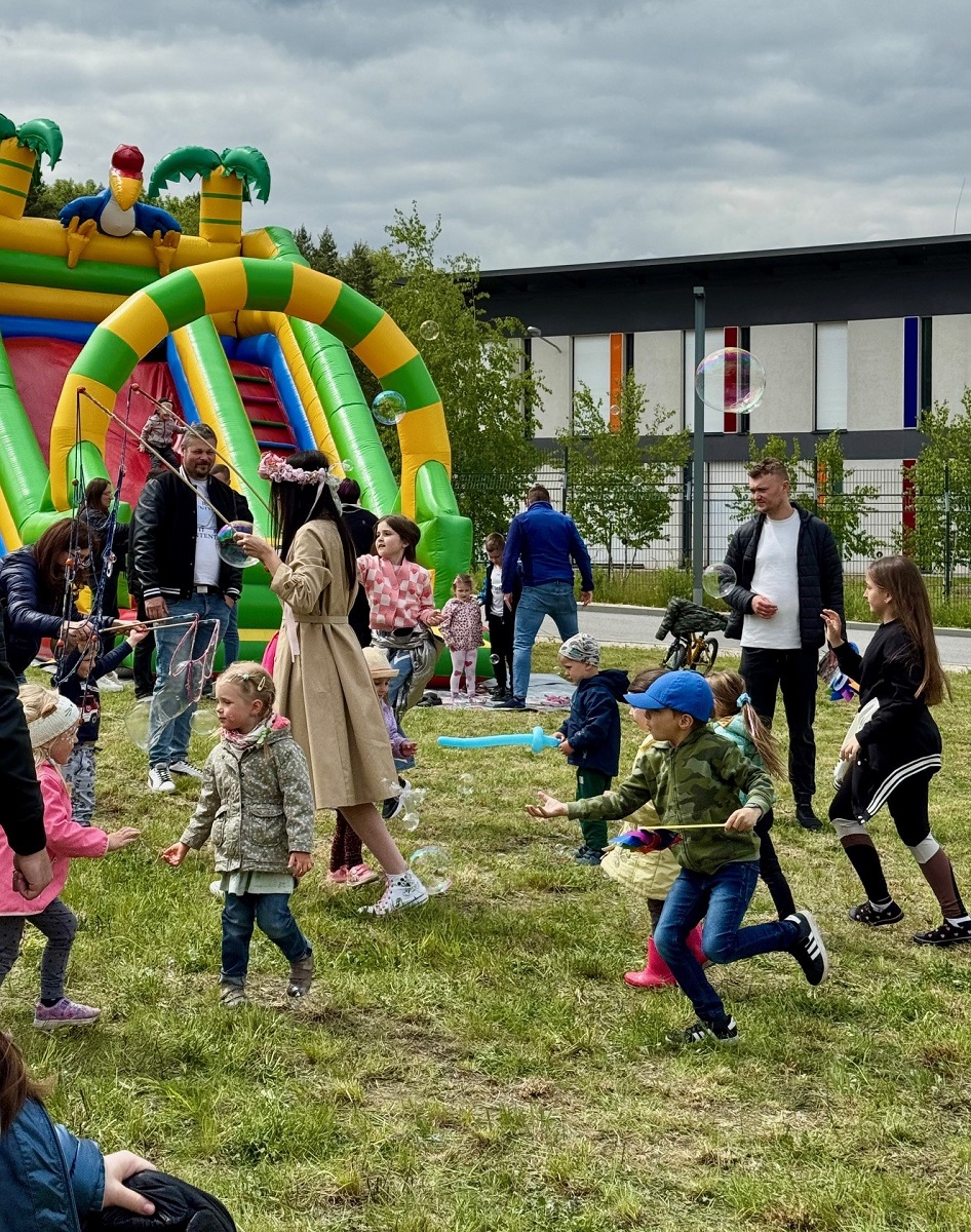 Dzieci i dorośli bawią się na trawie, w pobliżu stoi duży dmuchaniec.