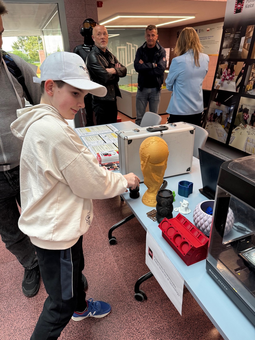 Chłopiec w jasnej bluzie i białej czapeczce przy stoisku z aktywnościami dla młodzieży