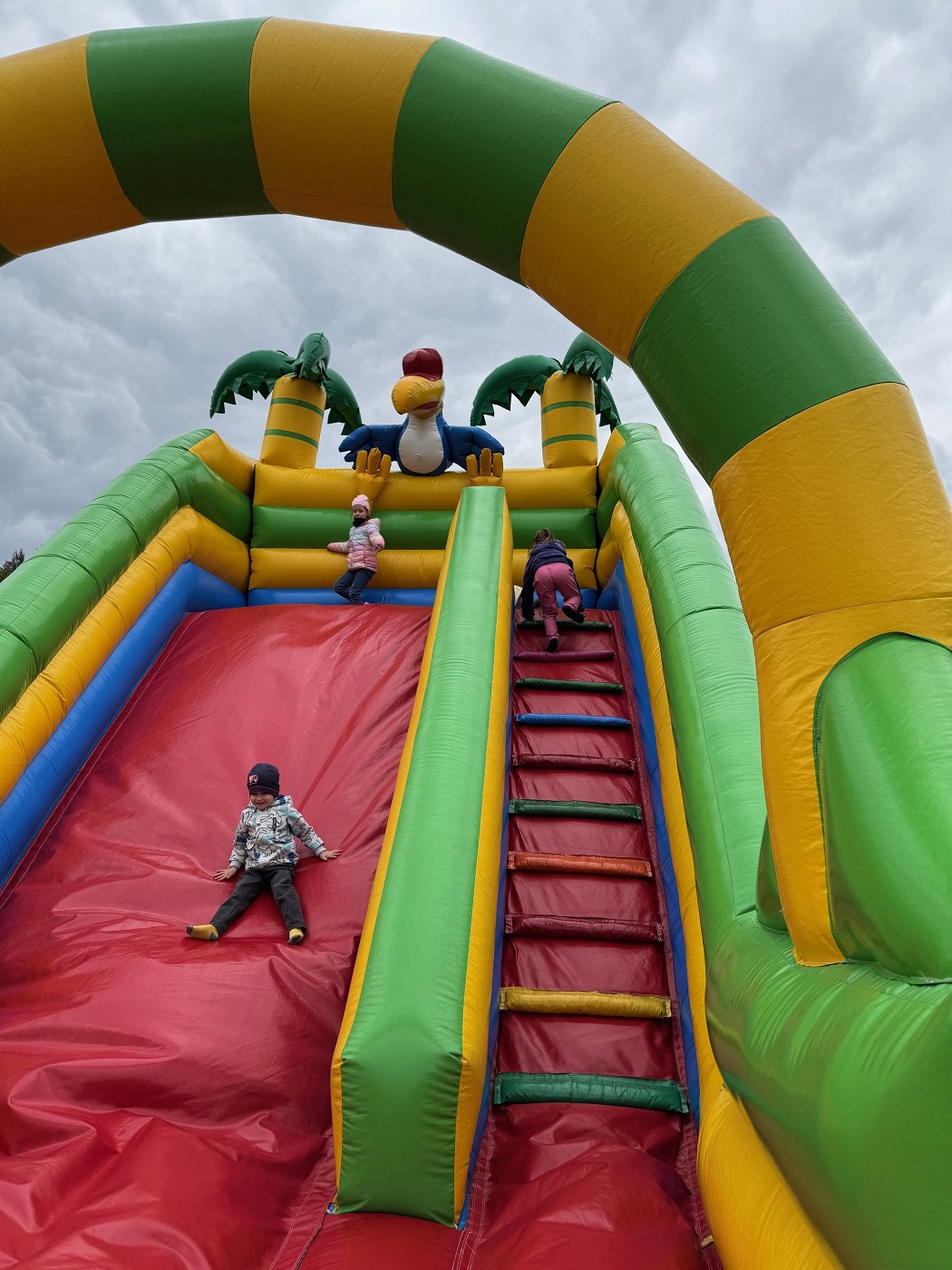 Dzieci zjeżdżają z góry na żółto-zielonym dmuchańcu