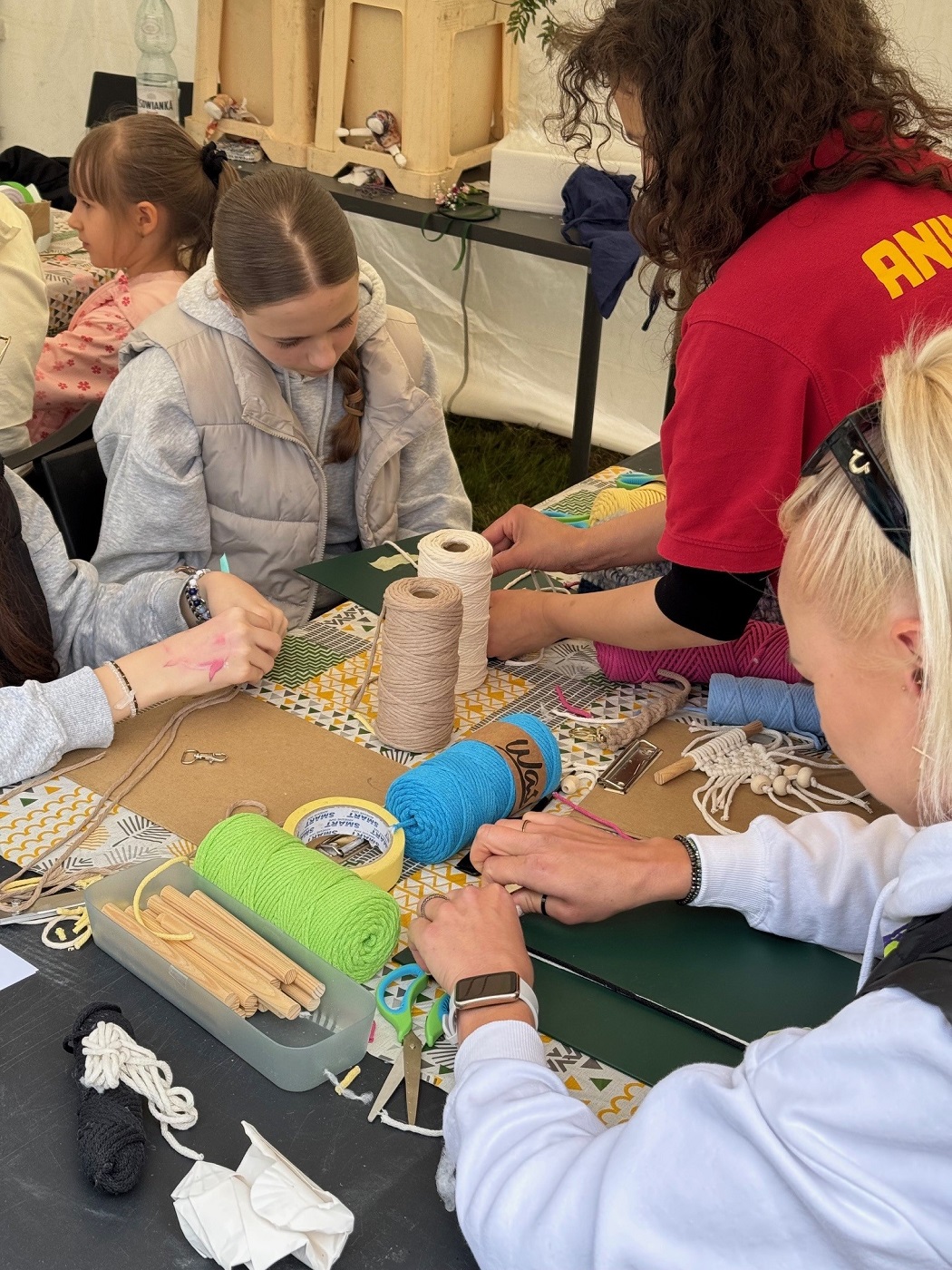 dziewczynki siedzą przy stole i biorą udział w zabawach z wykorzystaniem włóczek i nici.