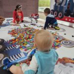 Dzieci bawią się na dużej planszy z klockami, na podłodze.