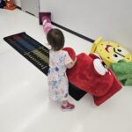 Mała dziewczynka trzyma w rękach dużą, czerwoną maskotkę.