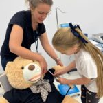 Kobieta i dziewczynka mierzą obwód ręki misia - maskotki.