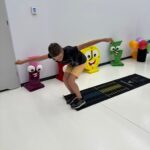 Chłopak w okularach na niedużej czarnej macie z podziałką pokazującą odległość skoku.