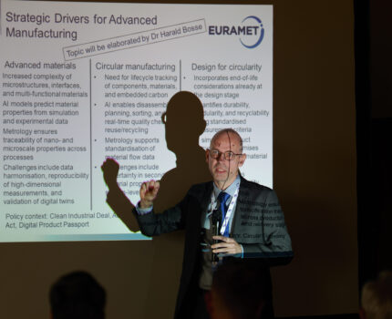 Łysy mężczyzna w okularach stoi przy prezentacji wyświetlanej na ekranie i gestykuluje.