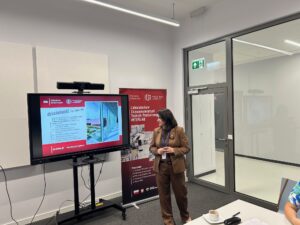 Kobieta stoi przy monitorze z wyświetloną prezentacją.