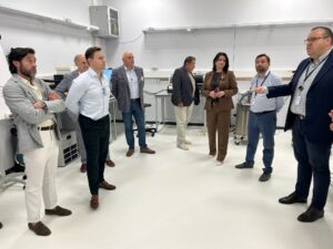 Kilka osób słucha gestykulującego mężczyzny w pomieszczeniu laboratoryjnym.