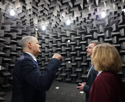 Trzy osoby stoją w pomieszczeniu zwanym komora bezechowa.