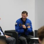 Trzech uśmiechniętych mężczyzn rozmawia, siedząc na ciemnych, skórzanych fotelach.