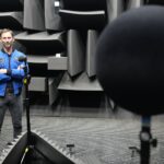 Mężczyzna w niebieskiej kurtce - Sławosz Uznański-Wiśniewski stoi w pomieszczeniu laboratoryjnym - komorze akustycznej