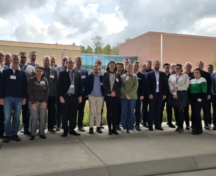 Grupa kilkudziesięciu osób pozuje do zdjęcia na terenie Kampusu GUM. W tle widoczne niewysokie budynki.