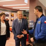 Dwóch mężczyzn i kobieta rozmawiają w oświetlonym korytarzu.