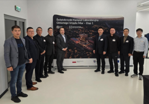 Dziewięć osób pozuje do zdjęcia na tle makiety Kampusu GUM.