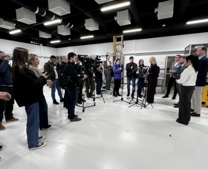 Grupa kilkunastu osób w pomieszczeniu laboratoryjnym. Widoczne ustawione mikrofony.