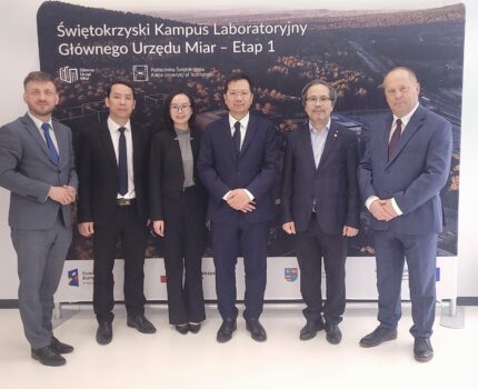 Pięciu mężczyzn i kobieta, ubranych w ciemnoszaro-granatowe garnitury pozuje do zdjęcia na tle makiety Kampusu.