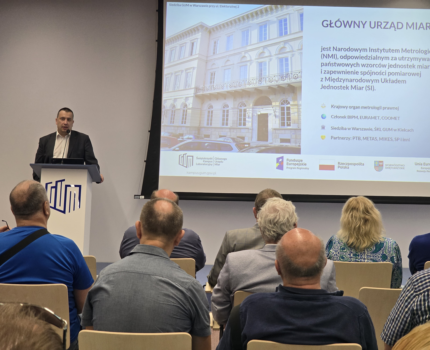Mężczyzna przy mównicy podczas prezentacji przed grupą osób siedzących na krzesłach w sali konferencyjnej. Obok z prawej strony widoczna prezentacja.