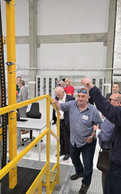 Grupa ludzi przygląda się dużym przyrządom pomiarowym stojącym w jasnym pomieszczeniu laboratoryjnym.